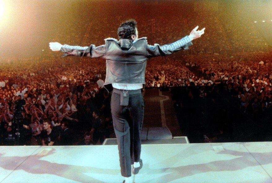 Michael Jackson de braços abertos para o público atrás durante performance de 'Heal The World' na 'HIStory World Tour'