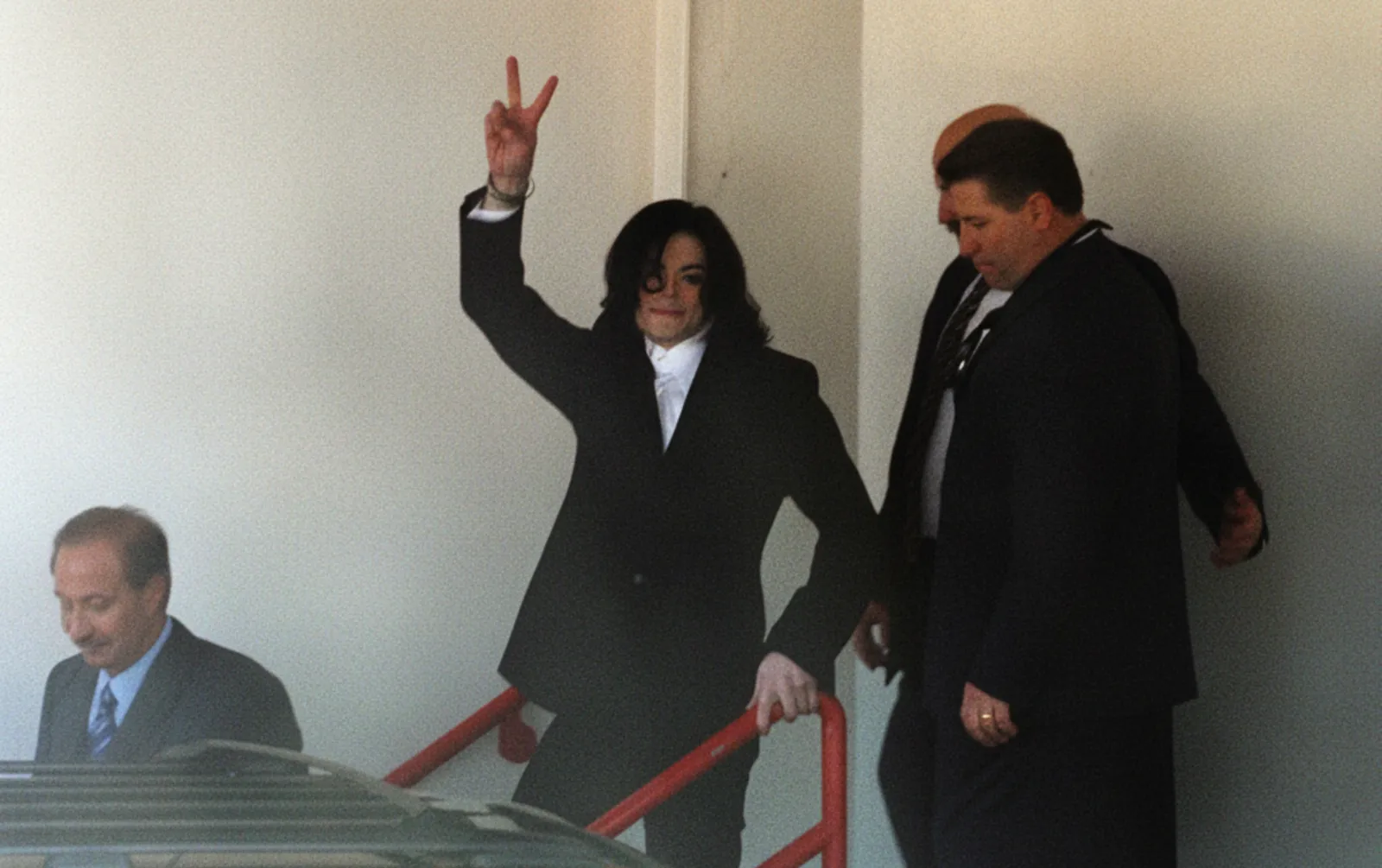 Michael Jackson acena após apresentar-se à Polícia em 2003 (à esquerda, Mark Geragos, advogado da época)